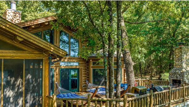 A log cabin with a deck, hammocks, and a stone fireplace.