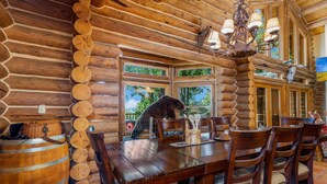 A rustic wooden dining area with a large table and chairs, a wooden barrel, and a log wall.
