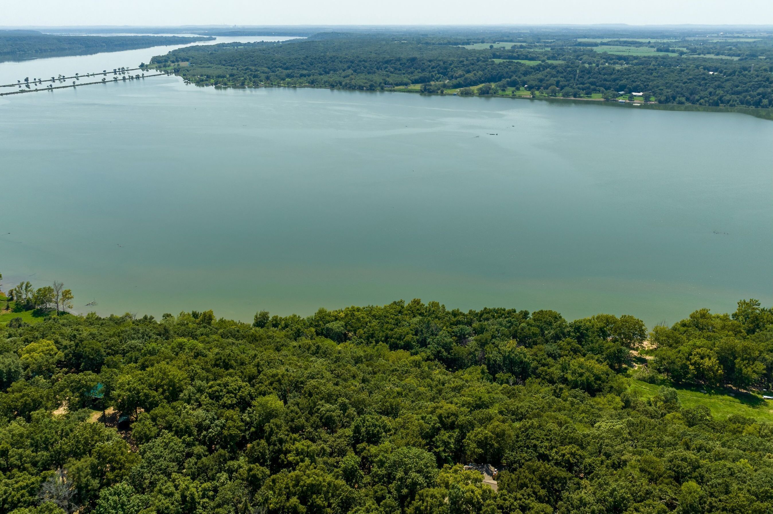 An aerial view of a large lake surrounded by dense forest. A bridge spans the lake, connecting two land masses.