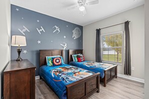 Un dormitorio con dos camas, un ventilador de techo, una ventana con cortinas y una pared decorada con calcomanías de Star Wars.