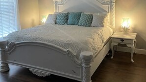A white ornate bed with a headboard, two bedside tables with lamps, and a ceiling fan in a room with wooden flooring. - Newly built house located on the bay (Pace)