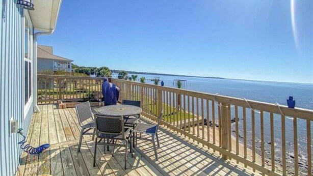 A wooden deck with a table and chairs, overlooking a beach and the ocean. - Newly built house located on the bay (Pace)