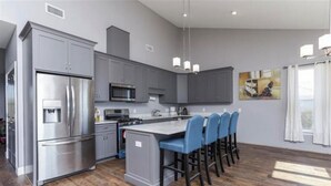 A modern kitchen with grey cabinets, stainless steel appliances, and a central island with bar stools. - Newly built house located on the bay (Pace)