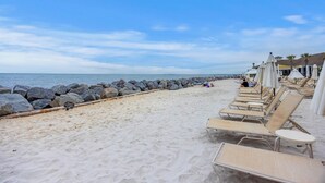 Una spiaggia con lettini, un molo roccioso e cielo sereno.
