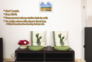 A room with a wall-mounted picture, a small table with a glass, and two decorative pillows.
