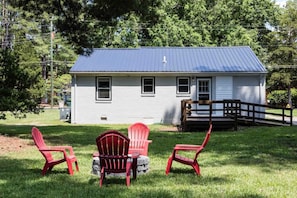 A small white house with a blue roof, surrounded by a grassy yard and trees. - 3BR Oasis | Mins from Downtown - King Bed (Garner)