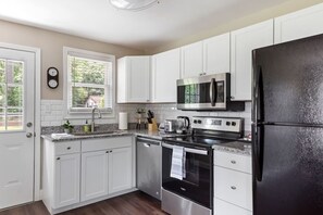 A modern kitchen with white cabinets, a stainless steel refrigerator, a microwave, a stove, and a dishwasher.