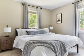 Une chambre à coucher avec un lit, deux tables de chevet, une lampe et une fenêtre avec des rideaux.