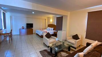 A hotel room with a bed, a TV, a desk, and two armchairs.