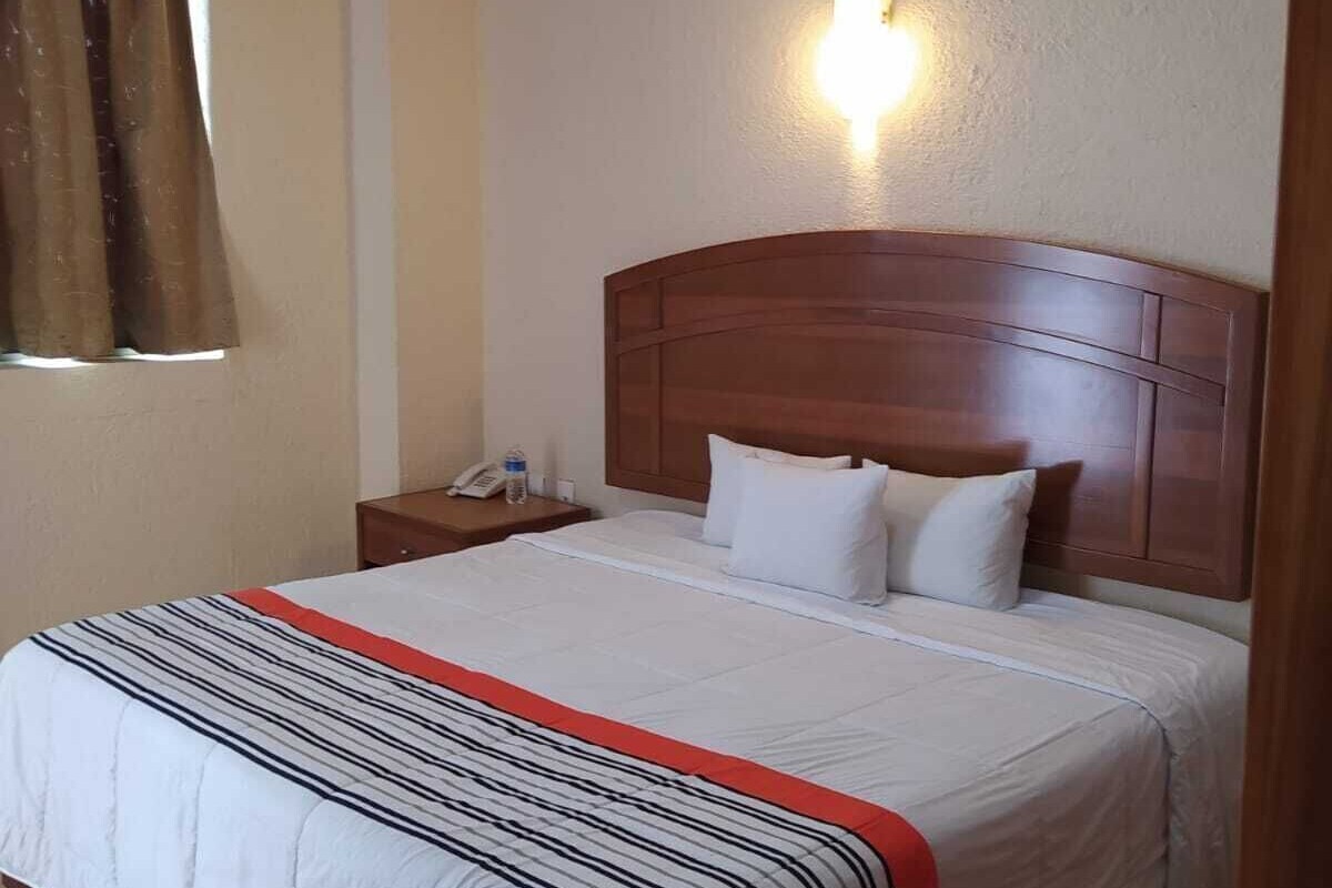A hotel room with a large bed, a nightstand, a telephone, and a wall-mounted light.