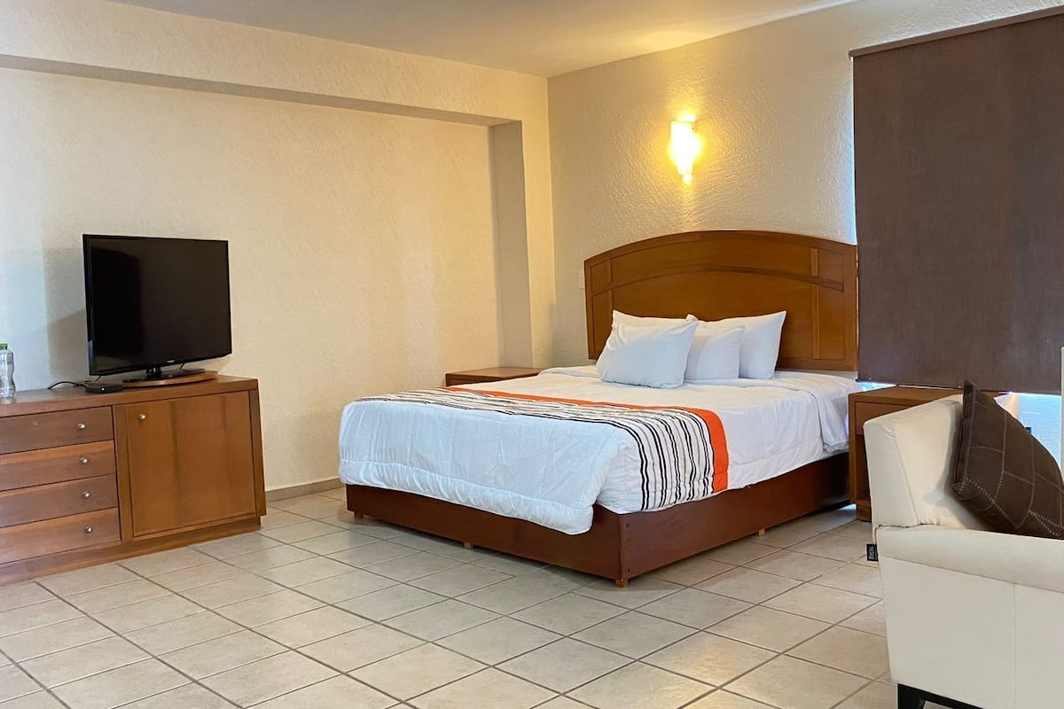 A hotel room with a bed, a TV, a wooden dresser, and a chair.