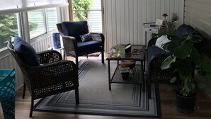 Eine überdachte Veranda mit Korbmöbeln, einem kleinen Tisch und einem Blumentopf.