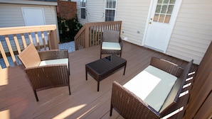 Una terraza de madera con mobiliario de mimbre y una puerta blanca.