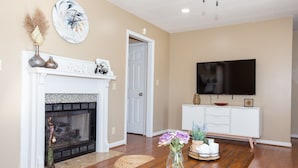 Una sala de estar con chimenea, televisor y mesa de comedor con un jarrón de flores.