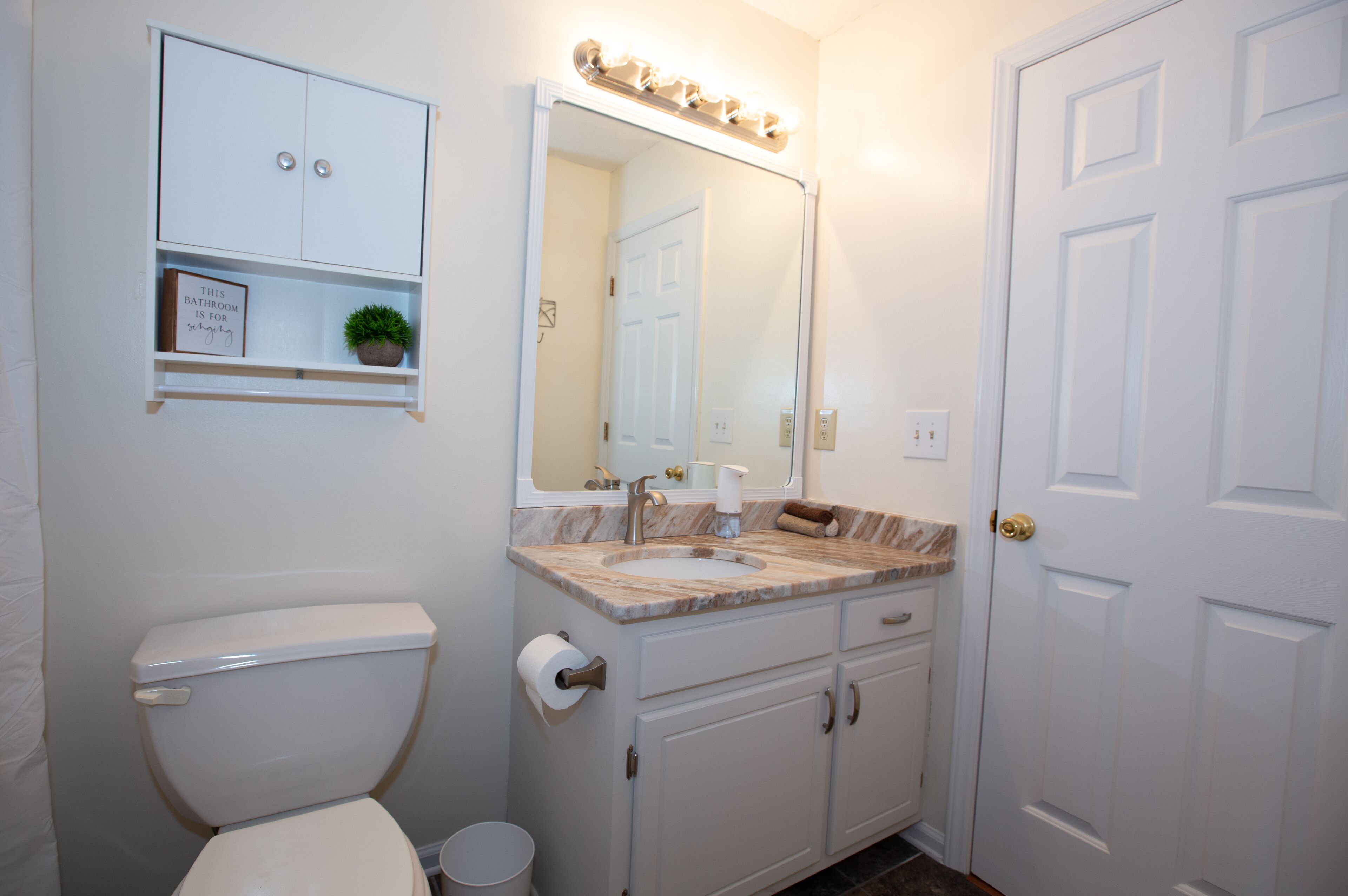 Une salle de bain équipée de toilettes, d’un lavabo, d’un miroir et d’un meuble de rangement.