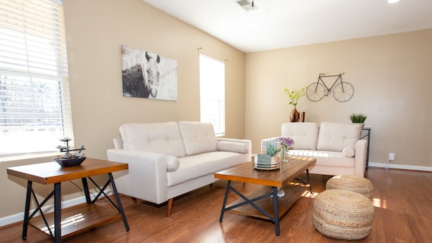 Una sala de estar con un sofá blanco, una mesa de centro de madera y un sillón blanco. Hay una bicicleta colgada en la pared y un jarrón con flores sobre la mesa de centro.