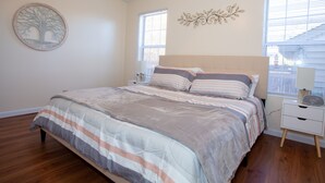 Un dormitorio con una cama, una mesita de noche, una obra de arte en la pared y una ventana.