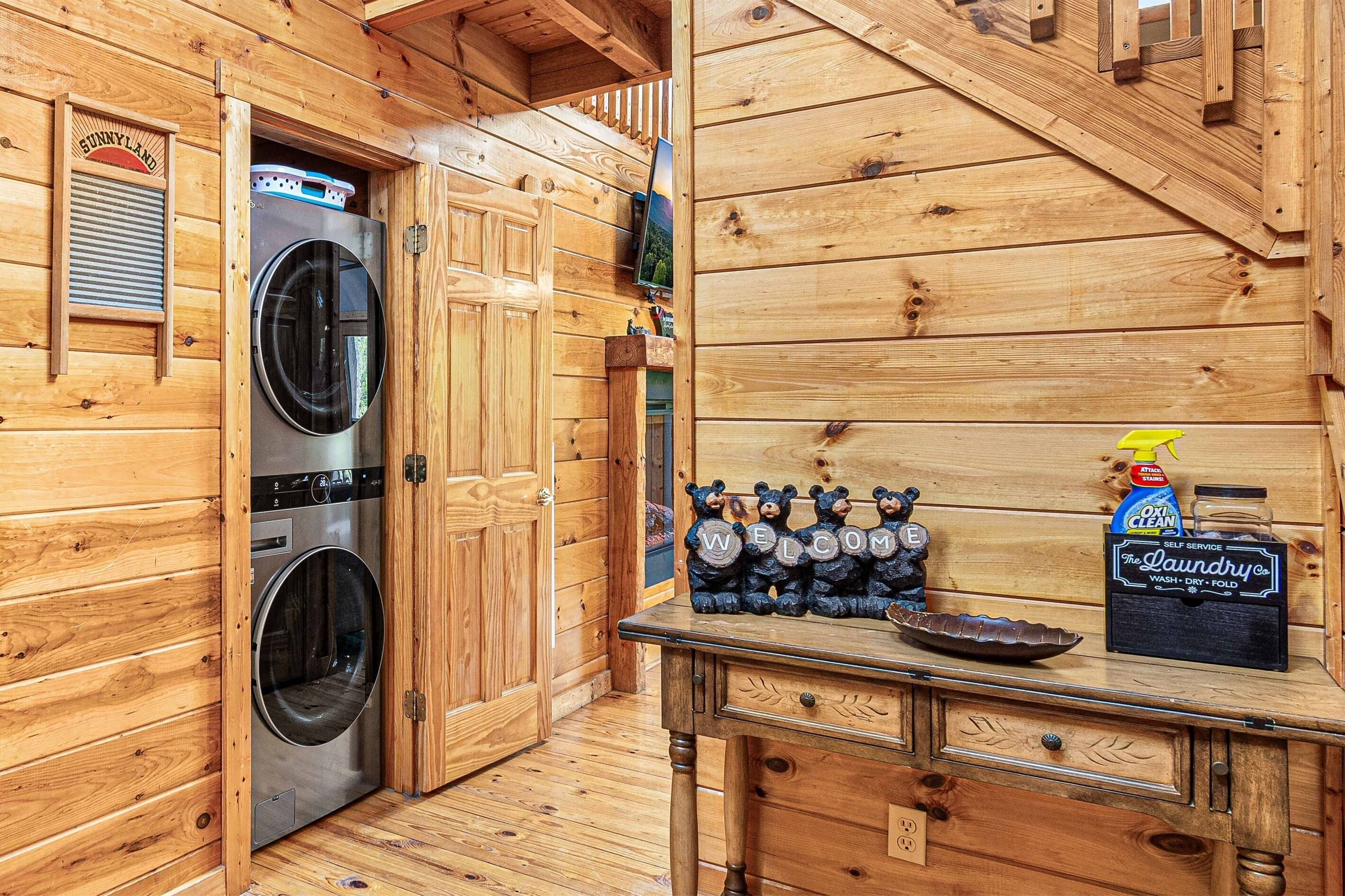 L’intérieur d’une cabane en bois, avec un lave-linge, un objet décoratif en forme d’ours et une boîte de lessive.