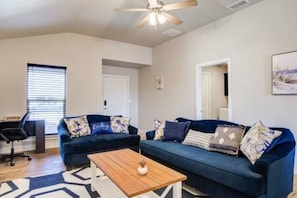 Un salon avec un canapé bleu, une table basse en bois et un ventilateur de plafond.
