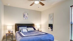 A bedroom with a bed, nightstands, a ceiling fan, and a window with blinds. - Milano Lodge - Cozy Retreat (Lubbock)