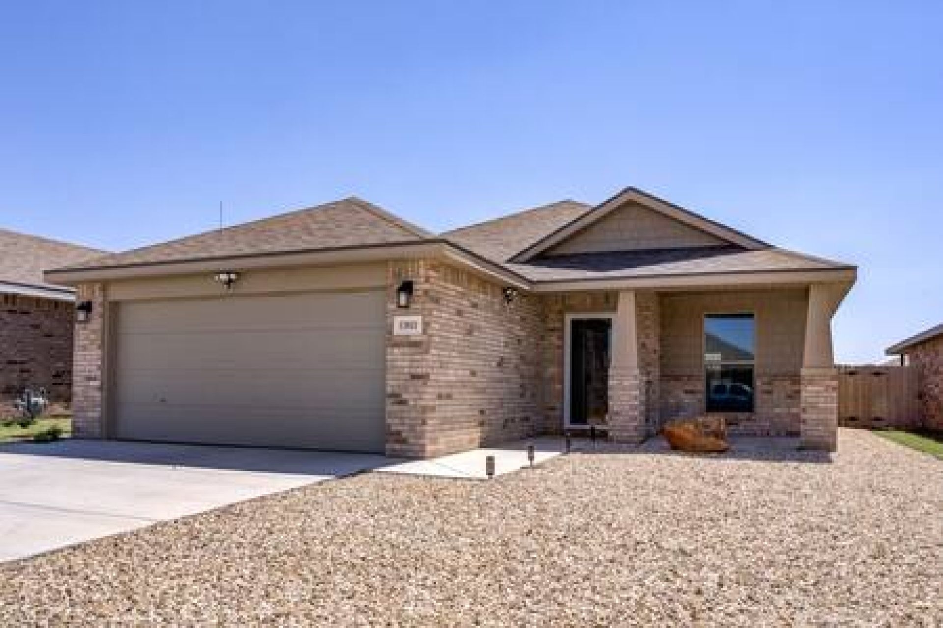 A single-story house with a garage, a front porch, and a gravel driveway.