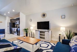 Una sala de estar moderna con televisor, sofá, mesa de centro y una cocina al fondo.