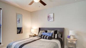 A bedroom with a bed, a ceiling fan, a nightstand, and a wall-mounted lamp. - Milano Lodge - Cozy Retreat (Lubbock)