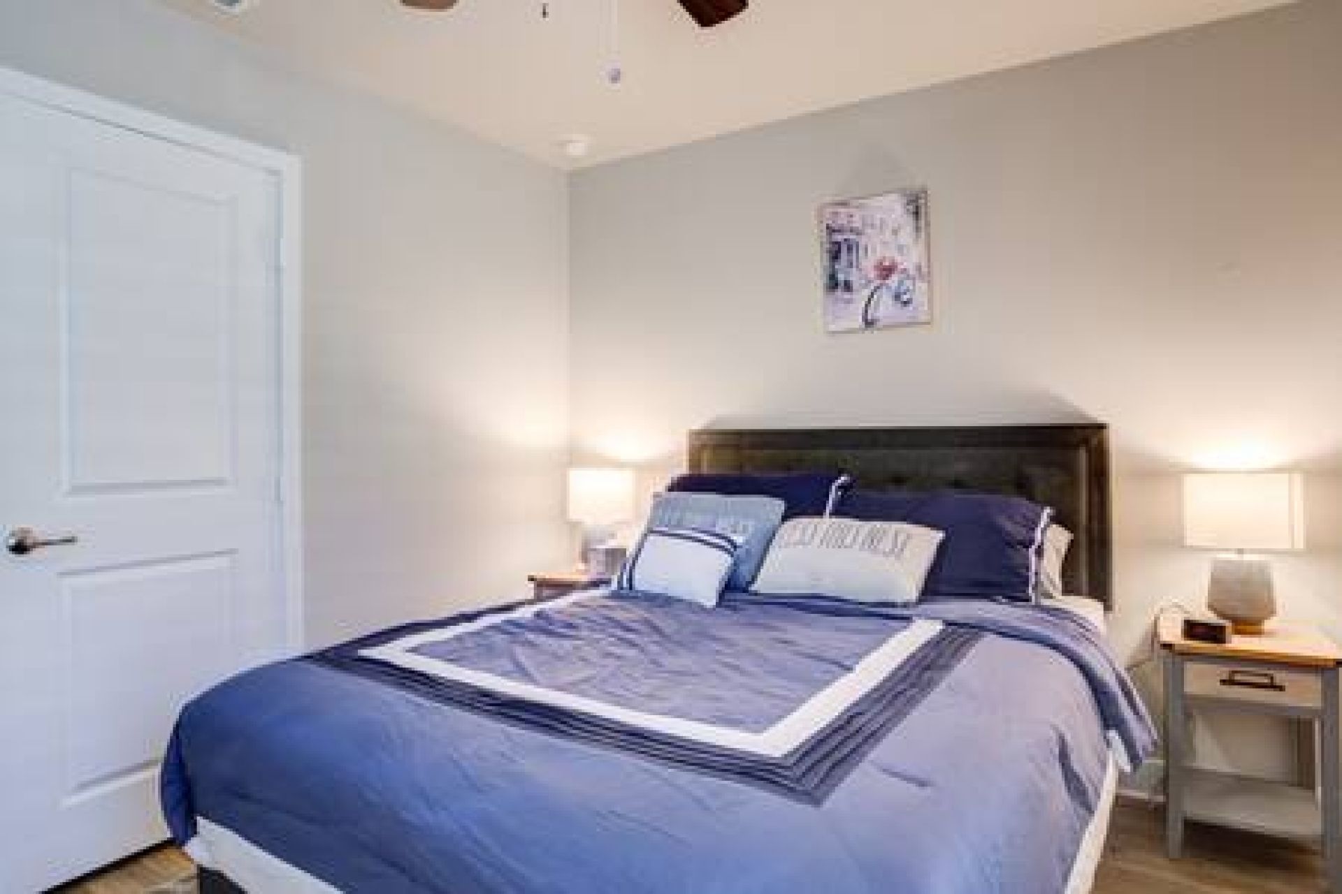 A bedroom with a bed, two bedside tables, a nightstand, a wall-mounted lamp, and a door.