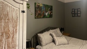 Ein Schlafzimmer mit einem Bett, einem Nachttisch, einer Lampe, einem Wandbild und einer Tür mit abblätternder Farbe.