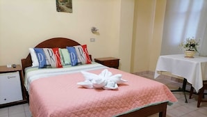 Una habitación de hotel con una cama, una mesita con un florero y una lámpara en la pared.