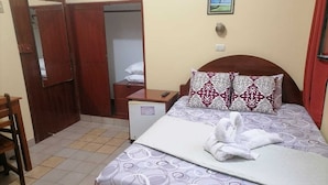 Una habitación de hotel con cama, escritorio, armario y un refrigerador pequeño.