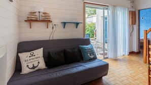 A cozy room with a dark grey sofa, a wooden shelf with decorative items, and a view of the outside. - Maison aux Oiseaux - Welkeys (Dolus-d'Oléron)