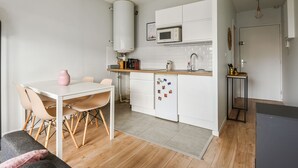 Une cuisine compacte avec des meubles blancs, un four à micro-ondes et une machine à café. On y trouve une table à manger avec des chaises et un petit tapis sur le sol.