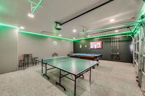 A room with a ping pong table, a pool table, and a projector.