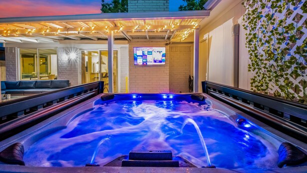 Un jacuzzi con caída de agua, rodeado por un porche cubierto con luces colgantes.