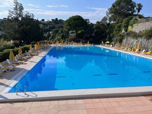 A rectangular swimming pool with clear blue water, surrounded by white lounge chairs and yellow umbrellas. - Appartement Mésangia - Welkeys (Villeneuve-Loubet)