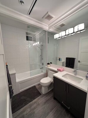 Ein modernes Badezimmer mit einer gläsernen Duschkabine, einer weißen Toilette, einem Waschtisch und einem großen Spiegel.