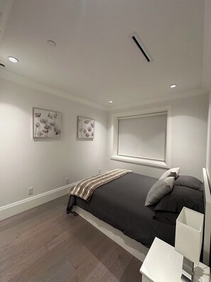 Ein modernes Schlafzimmer mit einem großen Bett, zwei an der Wand befestigten Kunstwerken, einem Fenster und einem Nachttisch.