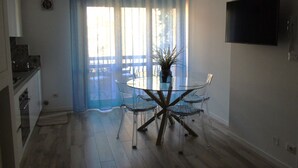A modern kitchen with a dining area featuring a glass table and chairs, a potted plant, and a TV mounted on the wall. - Medusa - Ground floor apartment, a few steps from the sea and the center (Pineto)
