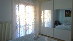 A bedroom with a bed, a wardrobe, a radiator, and a window with curtains. - Medusa - Ground floor apartment, a few steps from the sea and the center (Pineto)