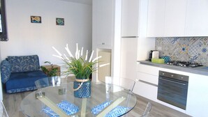 A modern kitchen with white cabinets, a stove, and a dishwasher. There is a glass dining table with blue patterned placemats and a potted plant. - Medusa - Ground floor apartment, a few steps from the sea and the center (Pineto)