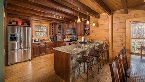 Una cocina amplia con armarios de madera, una isla grande con taburetes de bar, electrodomésticos de acero inoxidable y una pared decorativa de piedra.