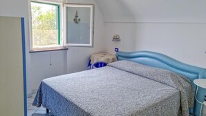 Een slaapkamer met een bed, een raam, een nachtkastje en een wandairconditioner.