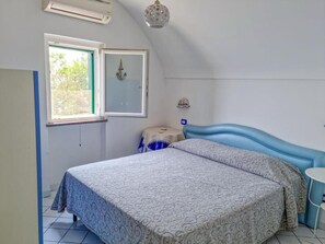 Une chambre à coucher avec un lit, une fenêtre, une table de chevet et un climatiseur fixé au mur.
