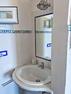 Une salle de bain avec un lavabo blanc, un miroir et un luminaire.