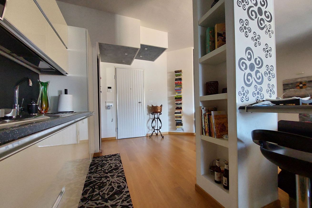 Una cucina moderna con un piano di lavoro, un tappeto decorativo e una libreria con libri e oggetti ornamentali.