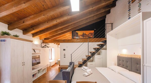 A hotel room with a wooden ceiling, a staircase, a bed, a TV, and a sofa. - Aly d’Angelo – alla Torre (Bardolino)