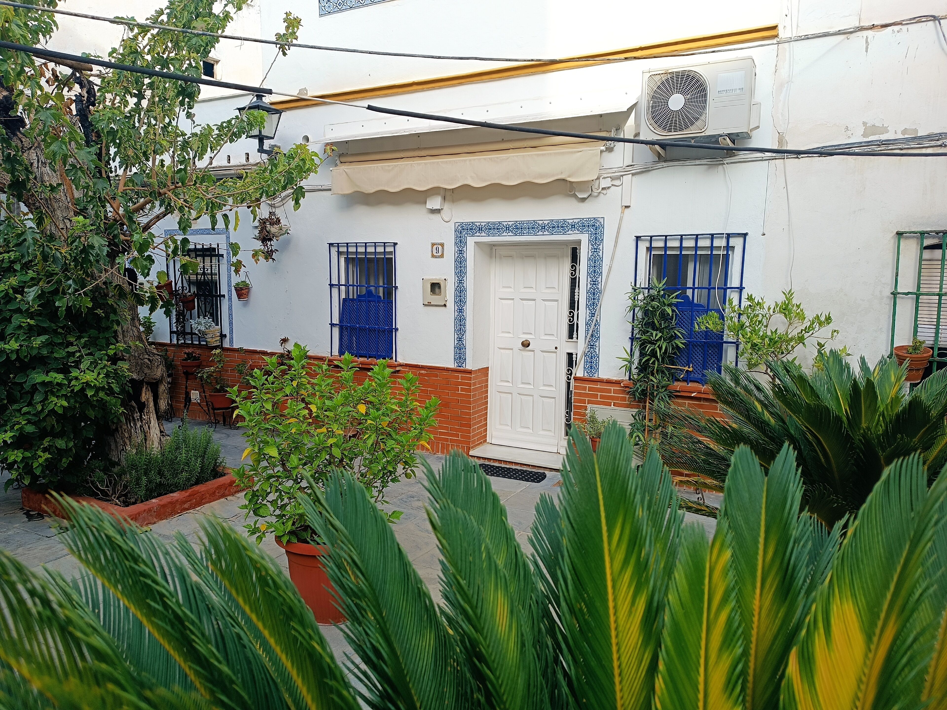 Um edifício branco com porta branca, grades azuis nas janelas e um pequeno aparelho de ar condicionado na parede.