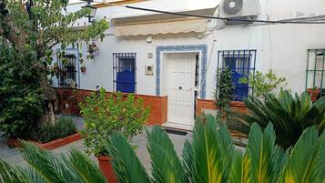 Um edifício branco com porta branca, grades azuis nas janelas e um pequeno aparelho de ar condicionado na parede.