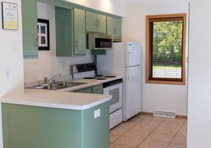 Kitchen area with central island, sink, stove, and refrigerator, offering a view of the surrounding greenery.